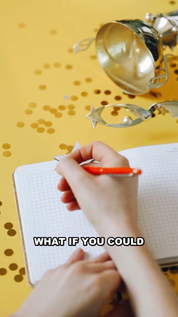 A hand writing in a notebook surrounded by golden confetti