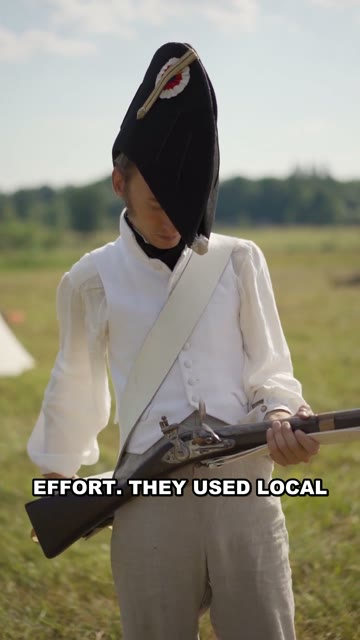 A reenactor in period military uniform holding a musket in a field